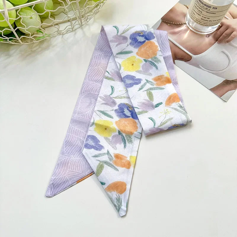 Une pile de foulards pour cheveux en soie élégants à motifs floraux violets, blancs et jaunes sur une surface blanche.