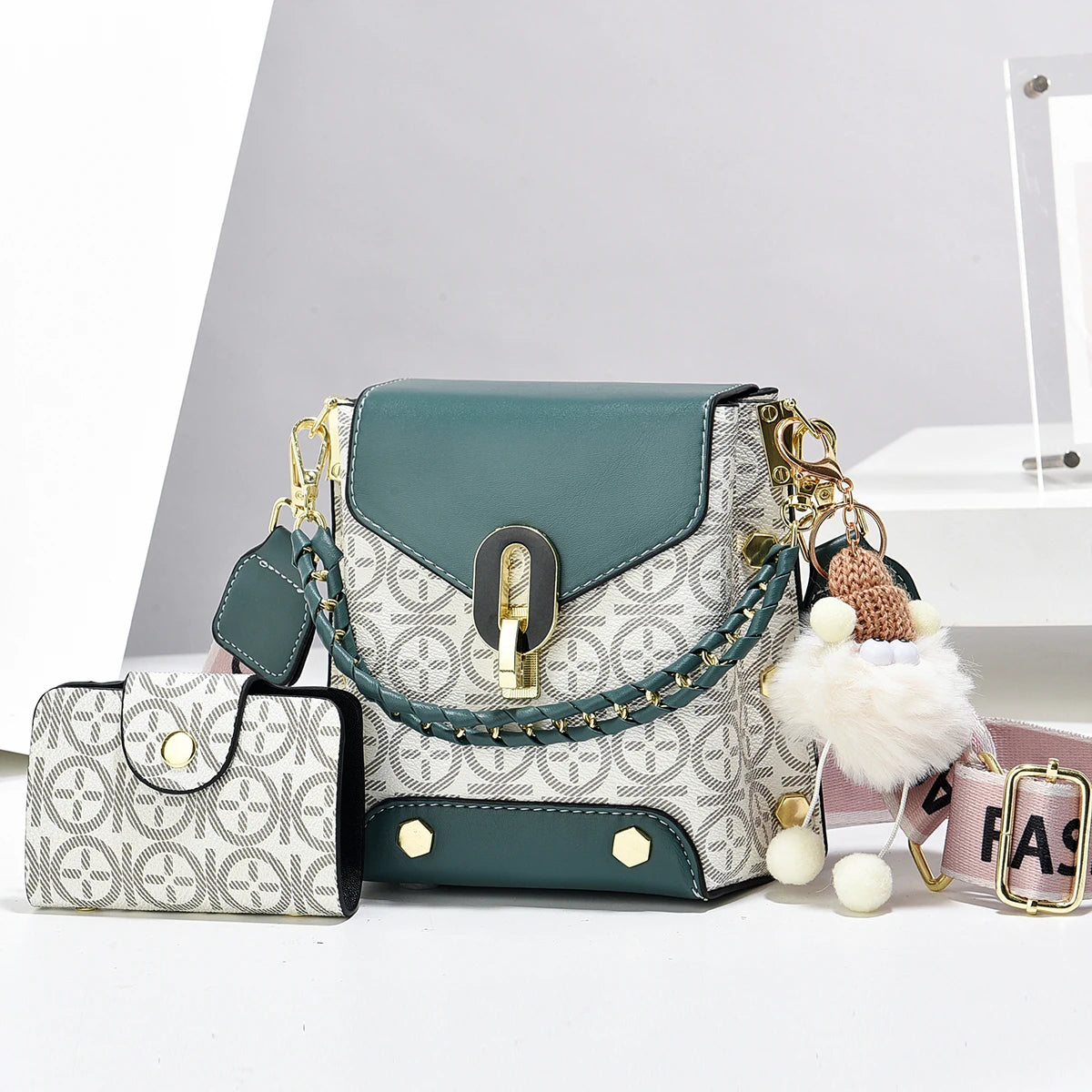 Sac bandoulière géométrique en similicuir teal et blanc avec quincaillerie dorée, présenté sur une surface blanche.