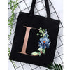 Black canvas tote bag featuring a large letter D and floral accents on a white grid background.