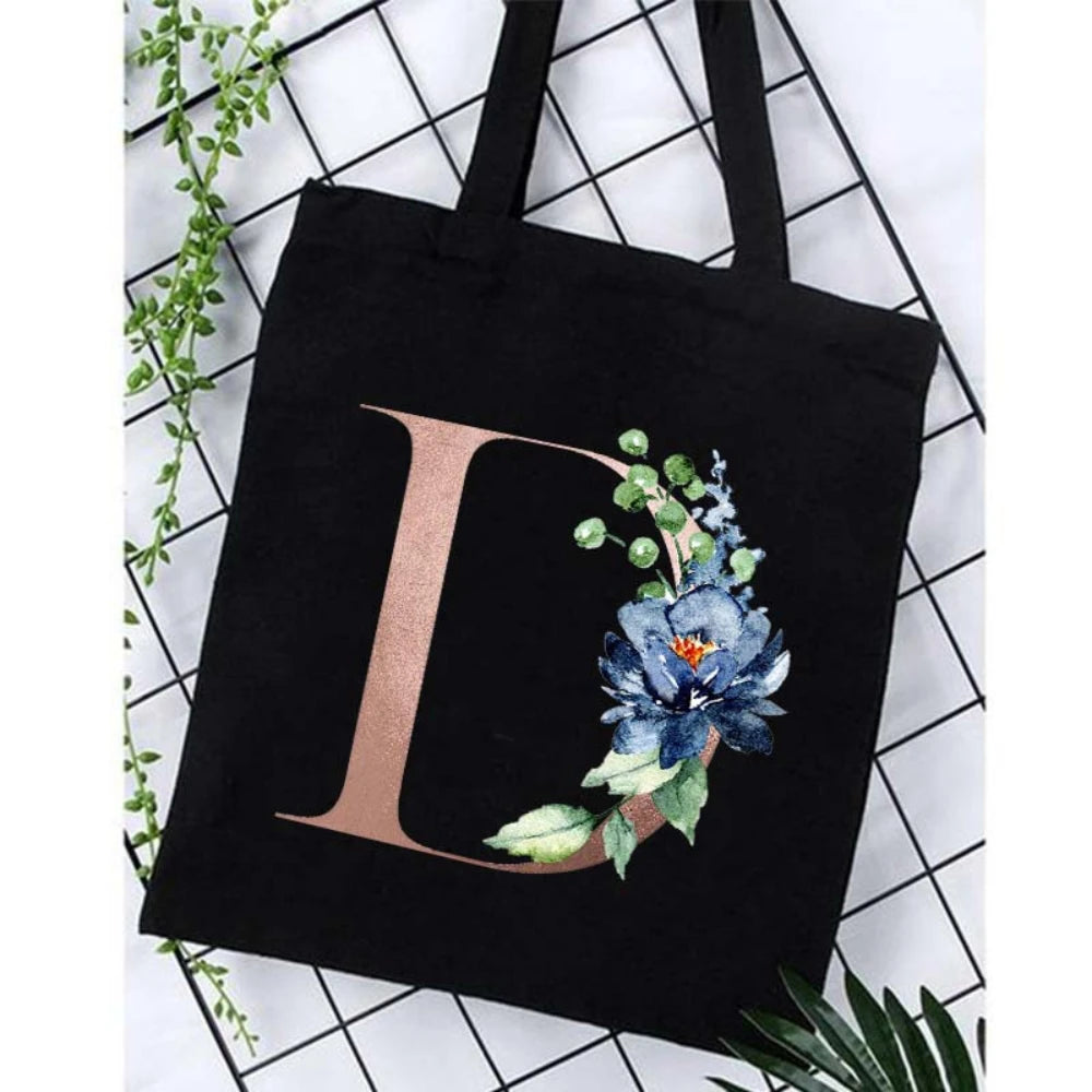 Black canvas tote bag featuring a large letter D and floral accents on a white grid background.