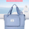 A light blue fashion travel bag with shoulder straps is displayed outdoors against a backdrop of the sea and sky.