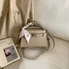A beige elegant PU leather crossbody clutch bag resting on a light-colored fabric.
