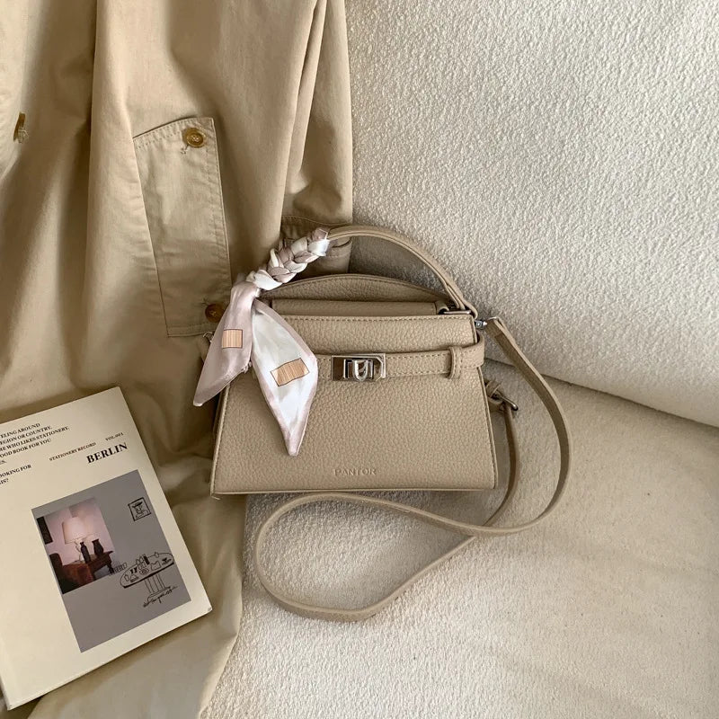 A beige elegant PU leather crossbody clutch bag resting on a light-colored fabric.