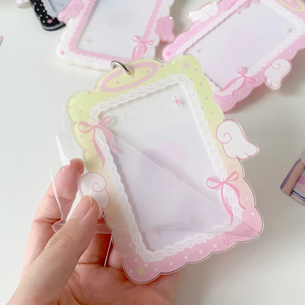 A hand holds a clear plastic photocard holder with pink and yellow decorative edges and angel wing cutouts.