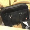 A black PU shoulder bag with a flap and strap is shown resting on a light wooden surface.