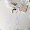 A white lace bow with pearl strands and black beads tied together as a keychain.