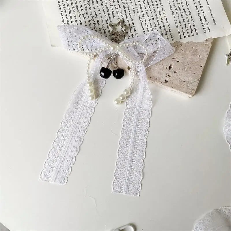 A white lace bow with pearl strands and black beads tied together as a keychain.