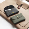 A beige leather card holder with a black and olive green personalized leather coin purse resting on it.