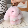 A pink fluffy rabbit plush charm attached to a gold keyring, resting on a light-colored paper.