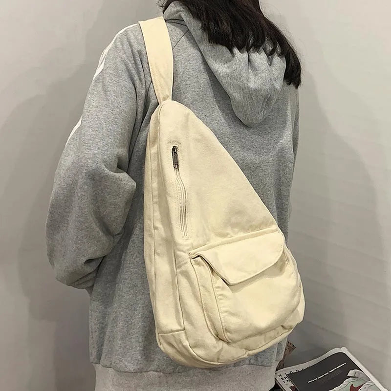 A light beige canvas crossbody shoulder bag worn by a person in a gray hoodie.