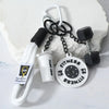 A white fitness dumbbell charm keychain with a black grip and chain is displayed on a white surface.
