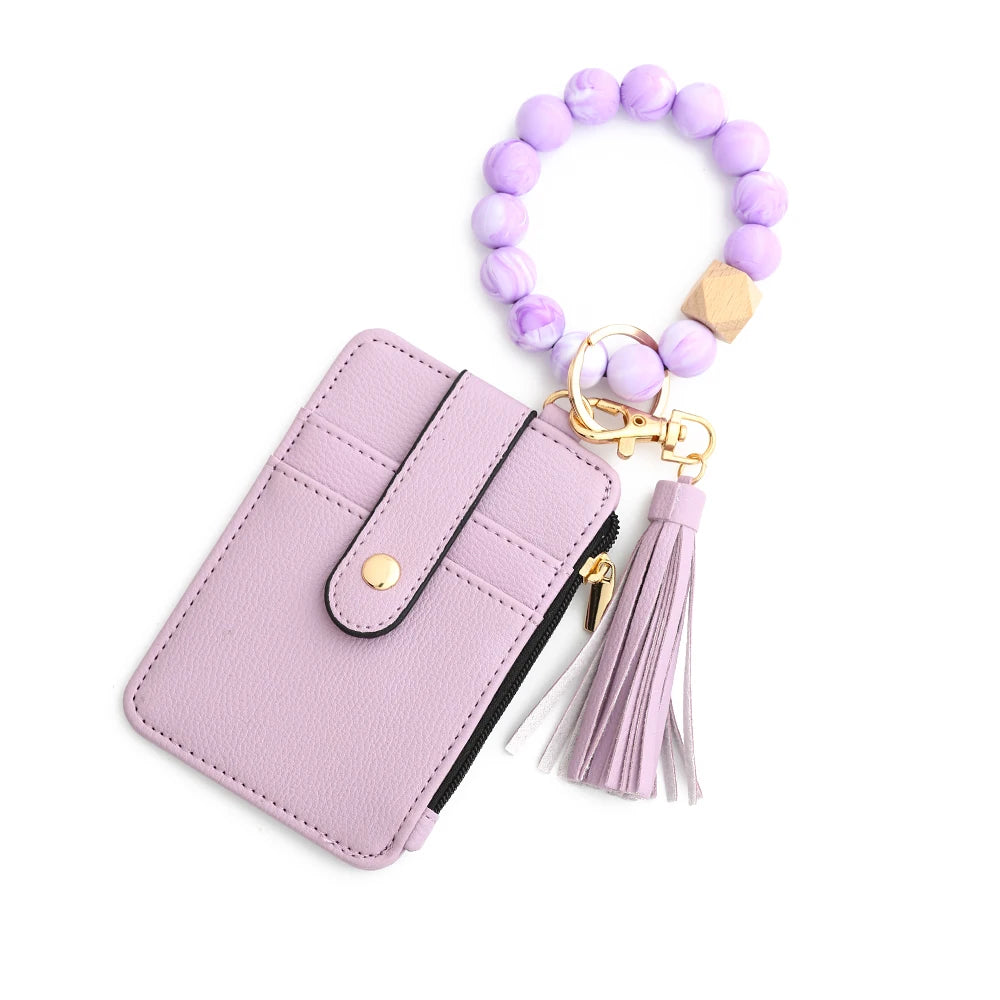 A light purple leather card holder with a gold keychain and a purple beaded bangle.