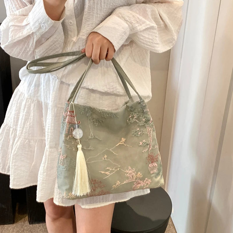 Una mujer sostiene un bolso de seda jacquard verde claro con bordado floral contra una blusa blanca.