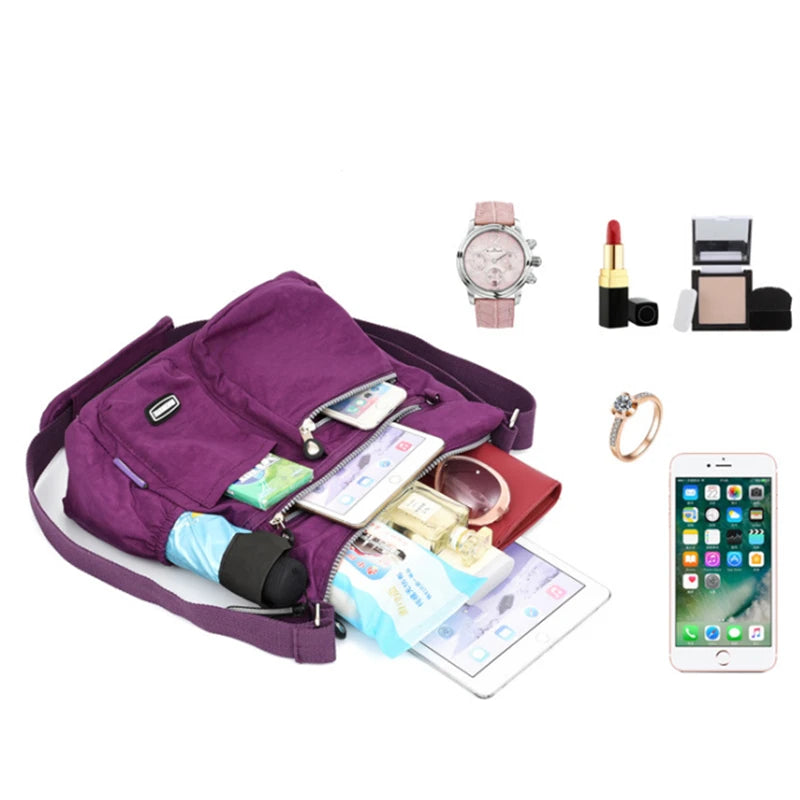 Lila Nylon-Crossbodytasche mit Accessoires wie Uhr, Lippenstift und Smartphone auf weißem Hintergrund