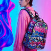 A woman wearing a pink shirt and a patterned backpack against a vibrant blue and pink background.
