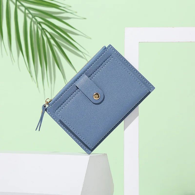 A light blue leather wallet with a flap closure and tassel detail is displayed against a pale green background.