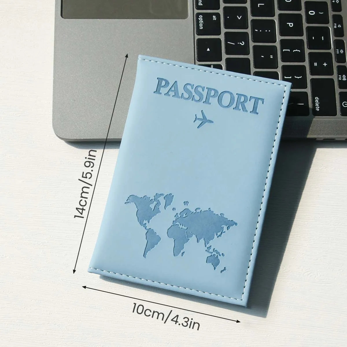 A light blue slim passport holder with a world map design placed on a white surface next to a laptop.