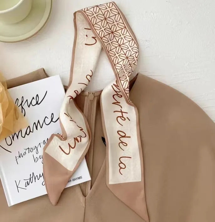 Un foulard pour les cheveux en soie beige, une fleur, un carnet et un tissu marron.