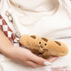 A hand holds a fluffy, light brown cartoon character plush toy against a white garment.