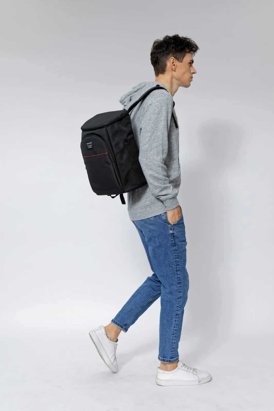 A person wearing a grey hoodie and jeans is carrying an olive green insulated thermal cooler backpack.