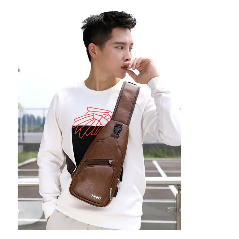 A young man wearing a white sweatshirt and carrying a brown leather chest bag with a headphone port.