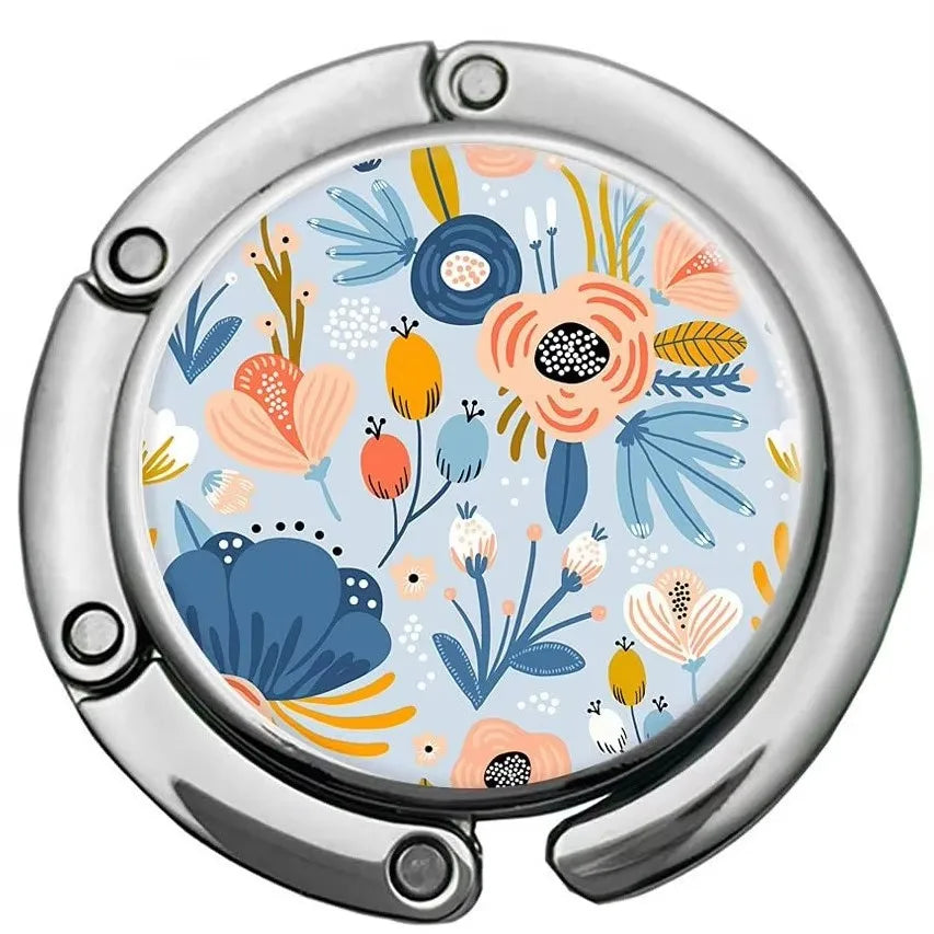A silver bag hook with a circular, multi-pattern floral design featuring blue, orange, and yellow elements.