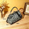 A black and white leopard print faux leather handbag with a top handle and crossbody strap resting on a wooden surface.