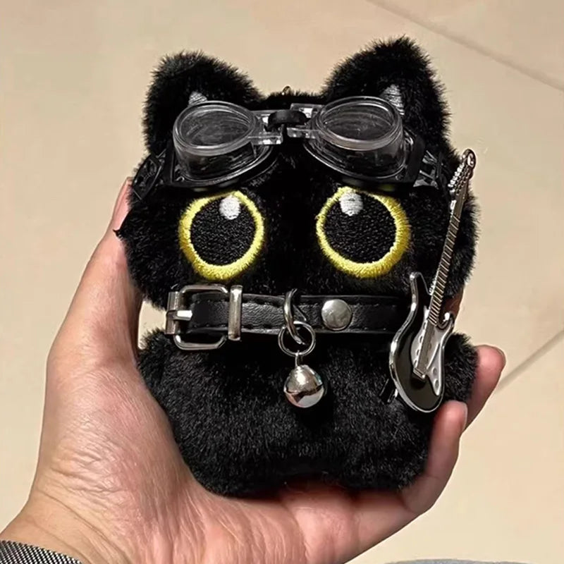 Colgante de peluche de gato negro con grandes ojos amarillos y una púa de guitarra plateada.