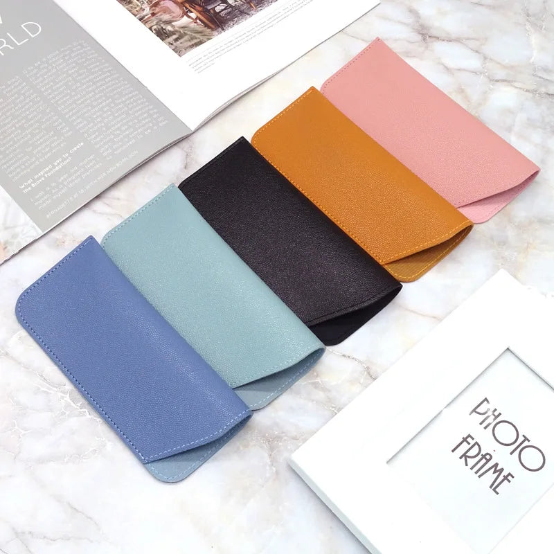 Una colección de fundas para gafas de cuero sintético rosa, naranja y azul dispuestas sobre una superficie de mármol.
