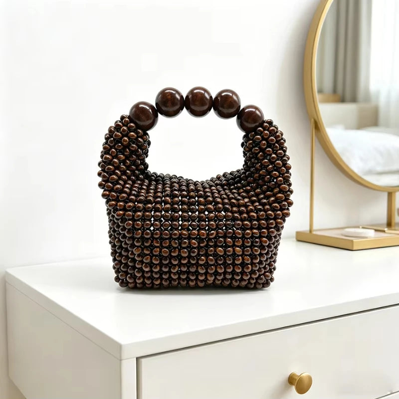 A dark brown beaded clutch bag with a textured surface and a round handle resting on a white cabinet.