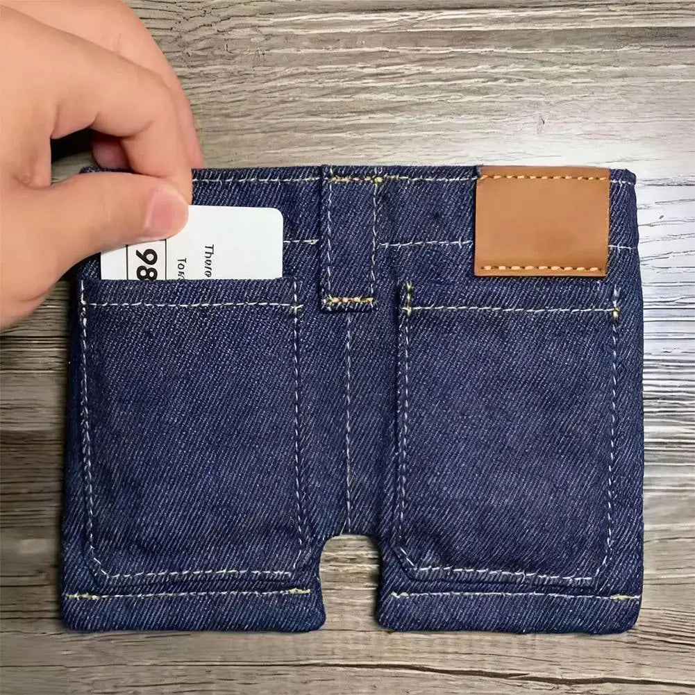 A close-up of a dark blue denim mini wallet and card holder with a leather patch on the top right pocket.