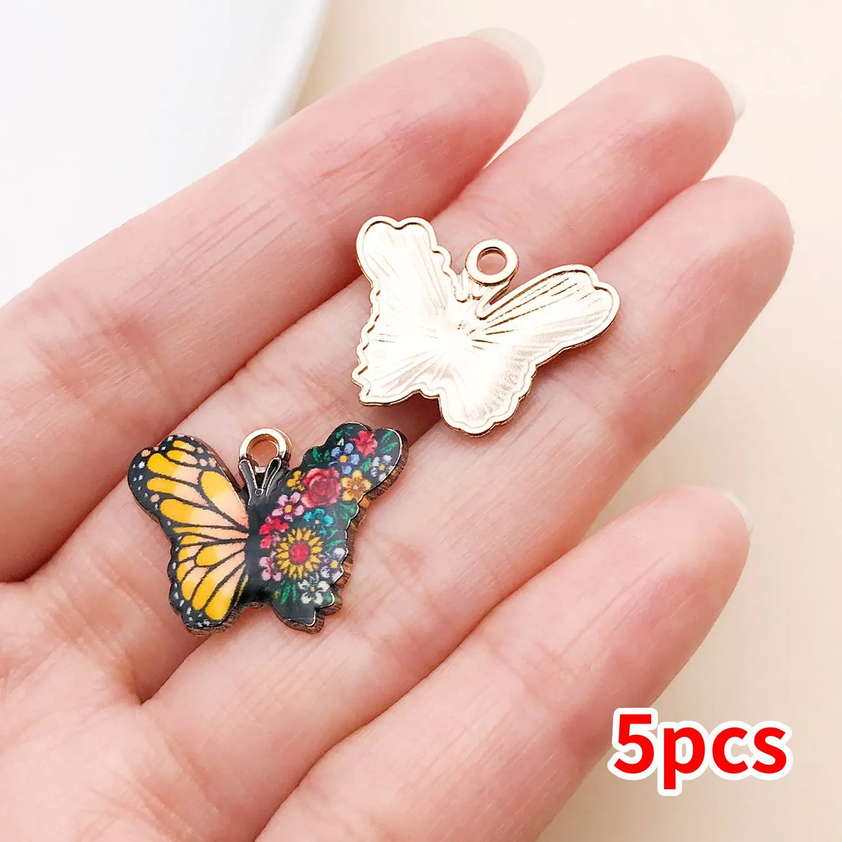 A set of five colorful butterfly enamel charms displayed on a person's hand.