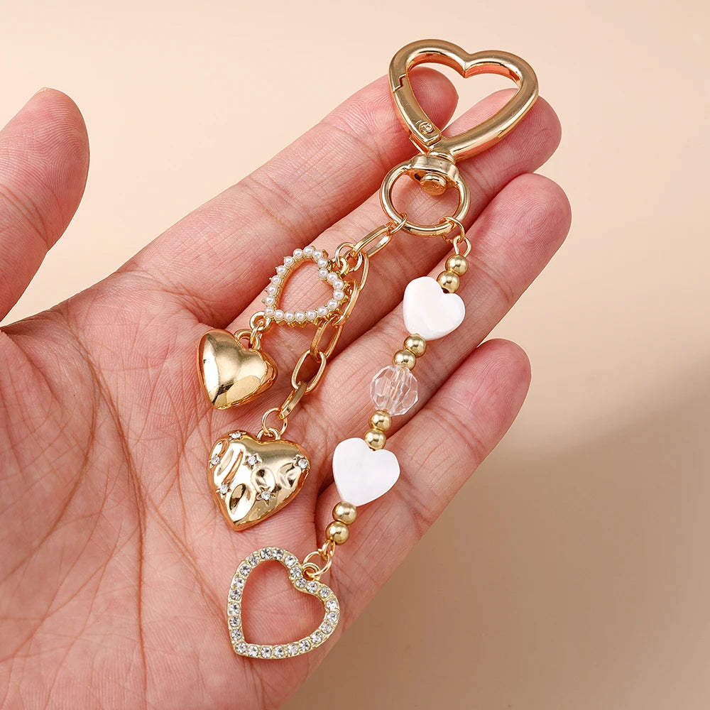 A gold-toned pearl bow heart keychain is shown being held in a hand against a light background.