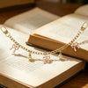 A gold chain necklace with pink bows and pearl charms draped across an open book.
