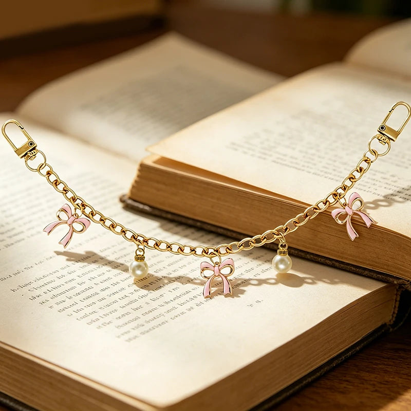 A gold chain necklace with pink bows and pearl charms draped across an open book.