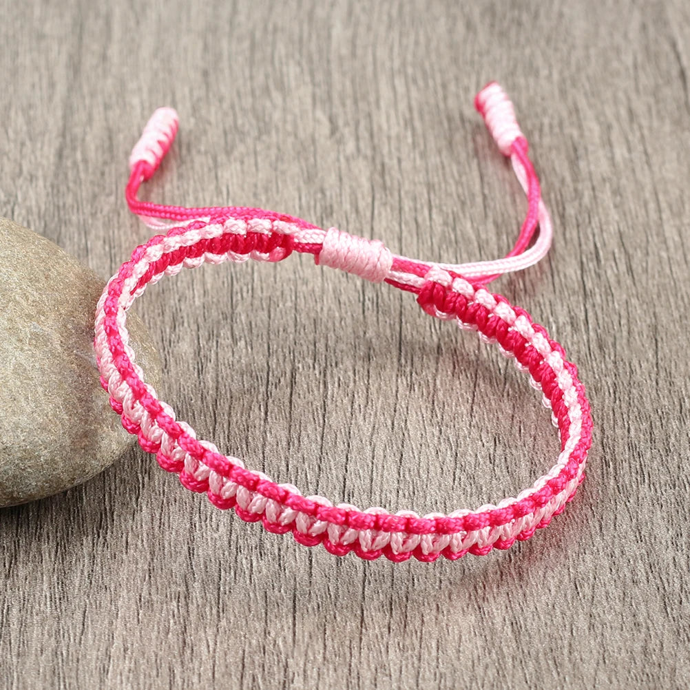 A pink and white braided rope bracelet is displayed on a gray wooden surface.