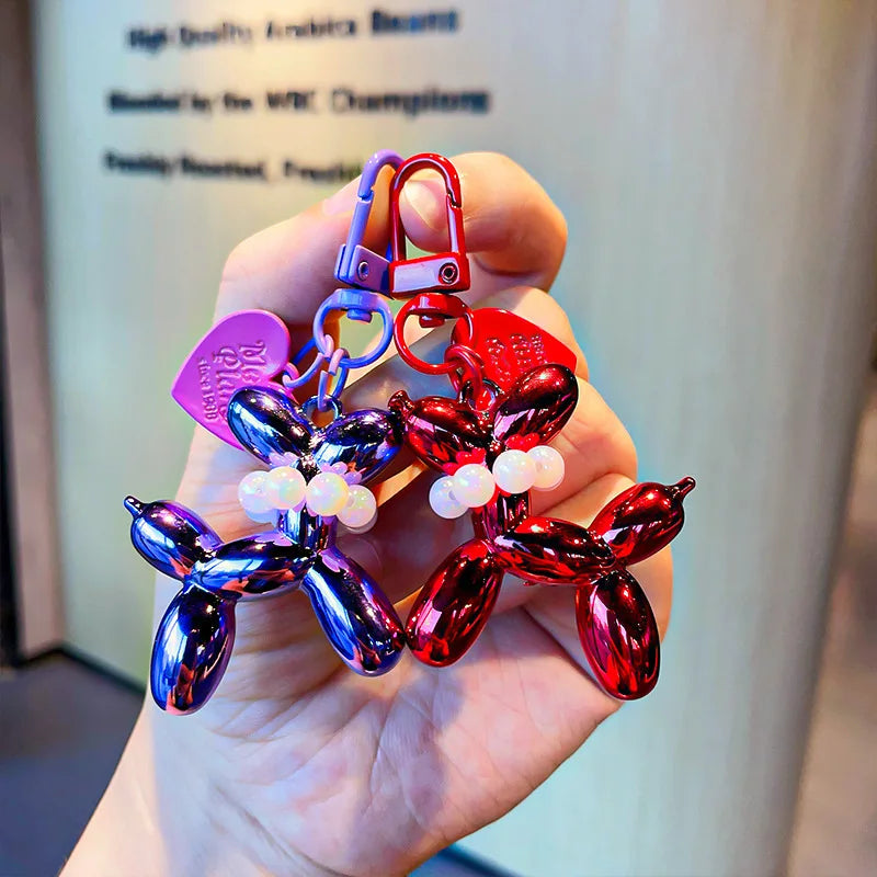 A hand holds a red and blue balloon dog keychain charm with a purple tag.