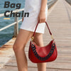 A woman is holding a red leather handbag with a black chain strap while walking on a wooden pier.