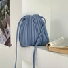 A light blue PU leather pleated crossbody bag hanging on a white shelf next to a stack of books.