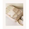 A beige fabric shoe organizer bag filled with white shoes, shown in a light neutral setting.