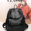 A black vintage soft leather backpack is shown against a light background with a woman in a red top in the background.