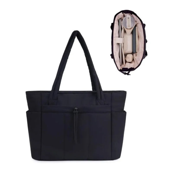 A black quilted tote bag with a light beige lining and a leather strap is shown against a white background.