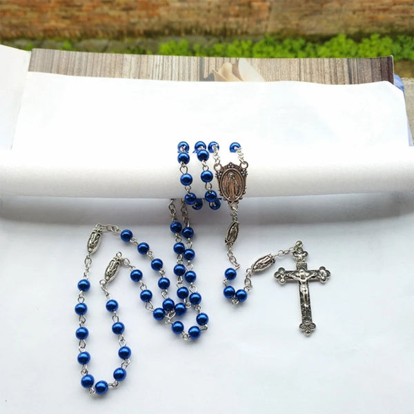 A blue rosary necklace featuring beads and a silver cross pendant displayed on white fabric.