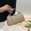 A hand holds a beige glitter crossbody evening clutch bag with gold chain details on a white textured surface.