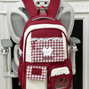 A maroon and white plaid backpack with a cat design and laptop compartment hanging on a white door.