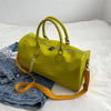 A lime green crocodile grain PU leather travel duffle bag with tan leather straps resting on a white bed next to denim jeans.