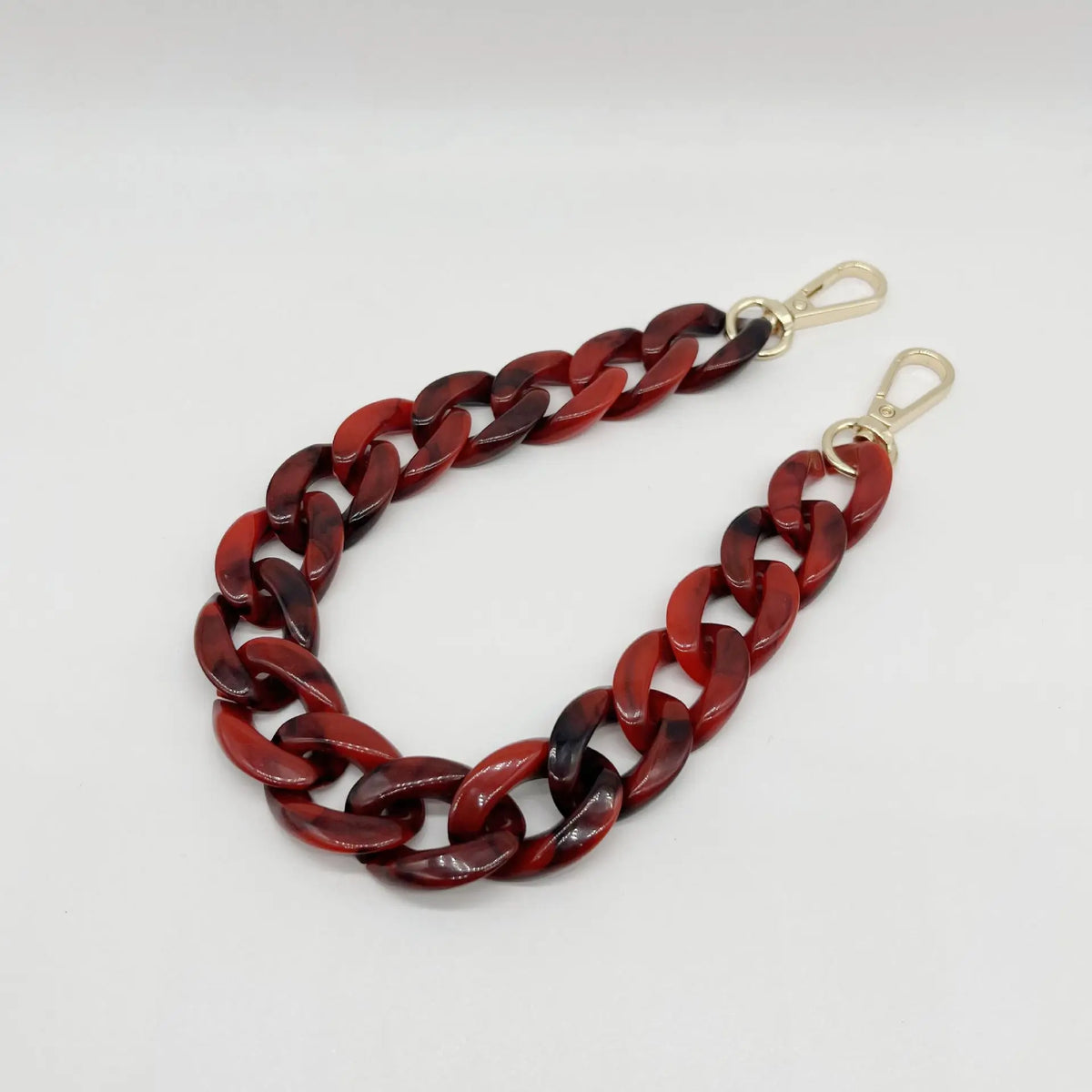 A close-up of a reddish-brown acrylic chain bracelet with gold-colored clasps.