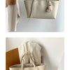 Sac cabas en cuir PU beige casual suspendu à un crochet contre un mur blanc.