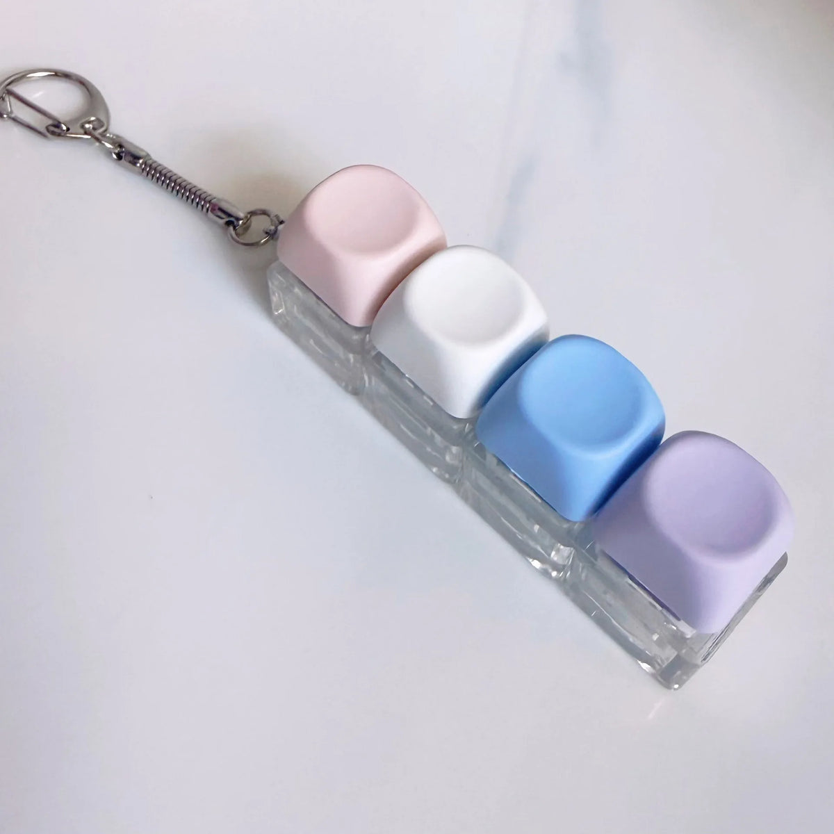 Clé-pendant anti-stress en plastique transparent avec cinq boutons en forme de macarons pastel sur un porte-clés argenté.