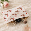 A beige corduroy cosmetic bag with a floral pattern and a gold zipper is shown next to makeup brushes and a bottle on a lace 